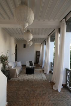 an outdoor living room with white curtains and brick flooring, along with two couches on either side of the patio