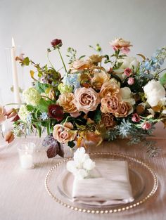 an arrangement of flowers on a table with candles and napkins in front of it