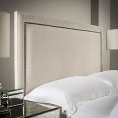 a bed with white sheets and pillows next to a night stand on a glass table