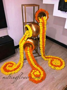 an arrangement of orange and yellow flowers on the floor next to a metal vase with two bells