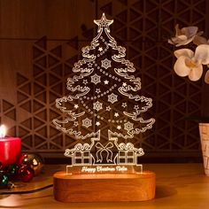 a lighted christmas tree sitting on top of a wooden table next to a lit candle