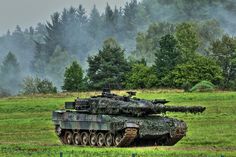 an army tank sitting on top of a lush green field in front of some trees