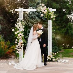 a bride and groom standing under an arch with flowers on it at the end of their wedding day