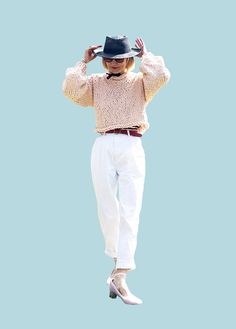 a woman wearing white pants and a black hat is standing in the air with her hands behind her head