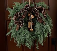 a wreath with pine cones and bells hanging on a door