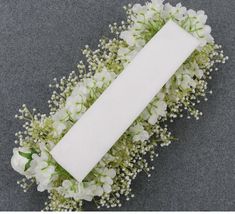 a white rectangular piece of paper sitting on top of flowers and greenery next to a gray background