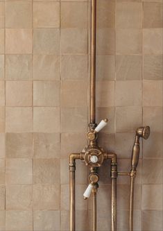 an old fashioned faucet in the corner of a tiled wall with pipes attached to it