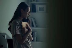 a woman holding a book in her hands and looking at the screen while standing next to a bookshelf