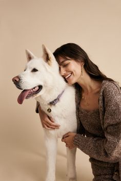 a woman is hugging her white dog on the side and she has it's tongue out