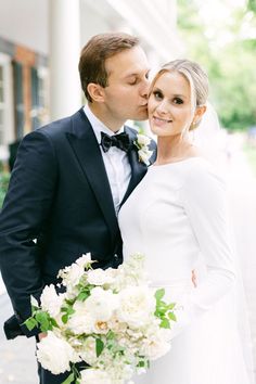 a bride and groom kissing in front of a white building with columns on the side