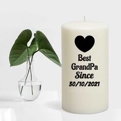 a white candle with a black heart on it next to a vase with a plant