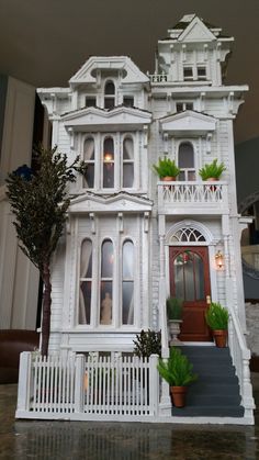 a large white doll house sitting on top of a table next to a potted plant