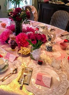 the table is set with pink flowers and teacups for two people to enjoy