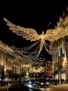 an angel statue is lit up in the middle of a city street at christmas time