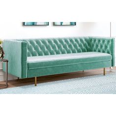 a green velvet couch with gold legs and tufted backrests in a living room