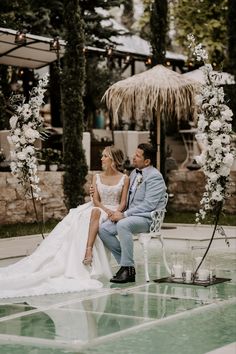 a bride and groom sitting on a bench in front of an outdoor wedding ceremony arch