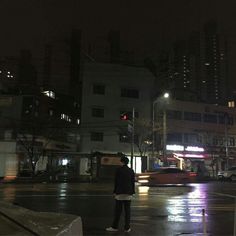 a man standing in the middle of a street at night with traffic lights and buildings behind him