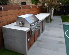 an outdoor bbq grill in the middle of a backyard with grass and brick walls