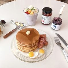 pancakes with eggs, bacon and jam on a plate next to some utensils