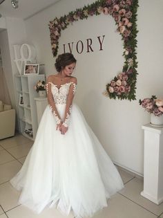 a woman in a white wedding dress standing next to a wall with flowers on it