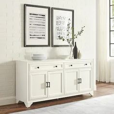 a white sideboard with two framed pictures on the wall next to it and a vase filled with flowers