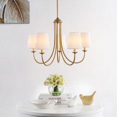 a chandelier hanging from the ceiling over a table with flowers and books on it