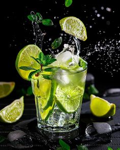 a glass filled with lemonade and limes on top of a black tablecloth