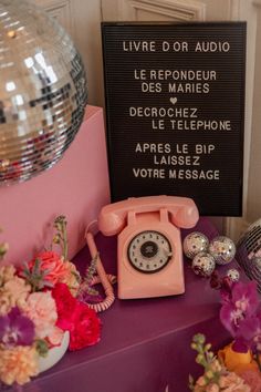 a pink telephone sitting on top of a purple table next to flowers and disco balls