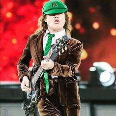 a man with a green hat and tie holding a guitar in front of a stage