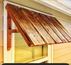 a wooden awning on the side of a house next to a window with grass in the background