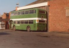 a green double decker bus parked in front of a brick building