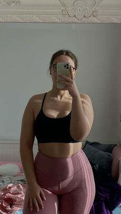 a woman taking a selfie in front of a mirror wearing pink pants and black bra top