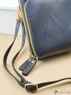 a blue purse sitting on top of a table next to a black bag with a gold zipper