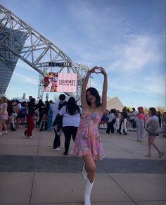 a woman in a short dress and knee high boots is making a heart with her hands