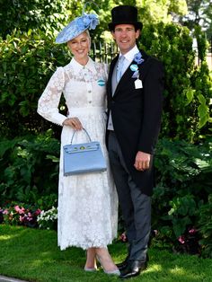 a man and woman standing next to each other in front of some bushes with flowers