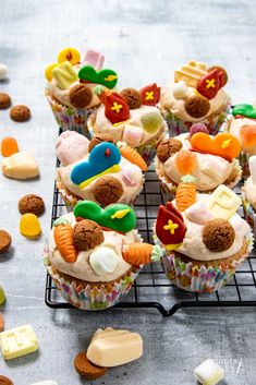 several cupcakes with frosting and various candies on a wire cooling rack