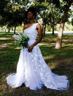 a woman in a white wedding dress holding a bouquet and posing for the camera with trees behind her