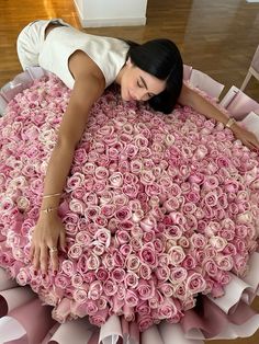 a woman laying on top of a giant bouquet of pink roses in the shape of a heart