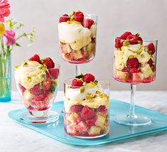 four glasses filled with desserts sitting on top of a blue tray next to flowers