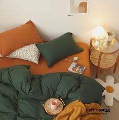 a bed with pillows and blankets on top of it next to a table with a lamp