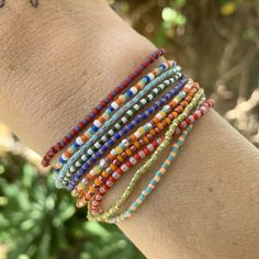 white luster, yellow, turquoise, red + white striped, purple and orange patterned seed beads strung on elastic please gently roll off and on to prolong its life handmade in venice, ca Stretch Beaded Bracelets Diy, Seed Bead Bracelet, Yellow Turquoise, Red And Purple, Purple And Orange, Beaded Bracelets Diy, Seed Bead Bracelets, Bead Stringing, Beaded Stretch Bracelet