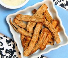 some fried food on a white plate next to a bowl of ranch dressing and a spoon