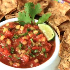 a white bowl filled with salsa surrounded by tortilla chips and cilantro