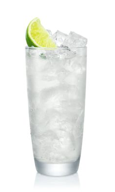 a tall glass filled with ice and lime wedged into the rim, on a white background