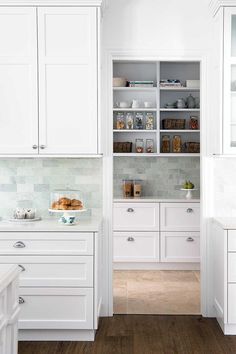 a white kitchen with wooden floors and cabinets in the center, along with an open pantry