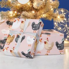 two presents wrapped in pink wrapping paper with chickens on them, under a christmas tree