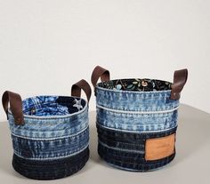 two denim storage baskets with leather handles on top of a table next to each other