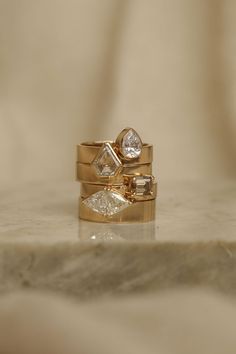 three gold wedding rings with diamond accents on a marble surface in front of a beige background