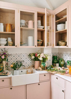 a kitchen filled with lots of pink cabinets and white counter tops next to a sink