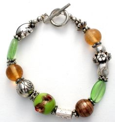 Fashion Jewellery - This is a bracelet with a green wedding cake bead, green and amber glass beads, and silver flowers, frog and spacers. It is 8" long, beads vary from 4mm to 17mm in width. Green Silver Beads For Jewelry Making, Green Beaded Bracelets With Large Beads As Gift, Green Beaded Bracelets With Silver Beads For Gifts, Silver Glass Beaded Bracelets With Large Beads, Elegant Green Beaded Bracelets With Large Beads, Green Nickel Free Bracelets With Round Beads, Green Bracelets With Spacer Beads, Green Bracelets With Silver Beads As Gift, Green Bohemian Beaded Bracelets With Silver Beads